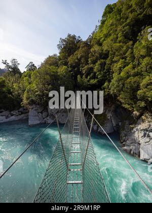 Die Hängebrücke aus Metall in der Caesspool Gorge führt über den türkisfarbenen, kristallklaren, blauen Wasserfluss am Arahura River an der Westküste der Südinsel Neuseeland Stockfoto