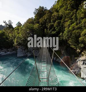 Die Hängebrücke aus Metall in der Caesspool Gorge führt über den türkisfarbenen, kristallklaren, blauen Wasserfluss am Arahura River an der Westküste der Südinsel Neuseeland Stockfoto