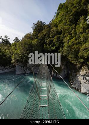 Die Hängebrücke aus Metall in der Caesspool Gorge führt über den türkisfarbenen, kristallklaren, blauen Wasserfluss am Arahura River an der Westküste der Südinsel Neuseeland Stockfoto