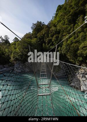 Die Hängebrücke aus Metall in der Caesspool Gorge führt über den türkisfarbenen, kristallklaren, blauen Wasserfluss am Arahura River an der Westküste der Südinsel Neuseeland Stockfoto