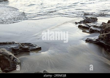 Nasse schwarze Sandformen an einem Strand zwischen Felsen Stockfoto