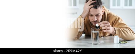 Ein Mann, der Medizin gegen Kater am Tisch in der Küche nimmt, Platz für Text. Bannerdesign Stockfoto