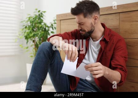 Trauriger Mann, der drinnen Fotos auf dem Boden reißt. Scheidungskonzept Stockfoto