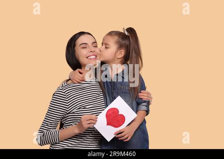 Glückliche Frau mit ihrer süßen Tochter und handgefertigter Grußkarte auf beigefarbenem Hintergrund, Platz für Text. Muttertagsfeier Stockfoto