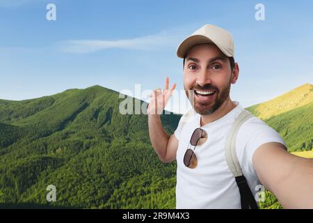 Ein lächelnder Mann, der Selfie macht und in den Bergen ein Friedenszeichen zeigt Stockfoto
