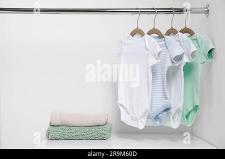 Kleiderbügel mit Babybekleidung und Kleiderstapel in der Nähe der weißen Wand. Platz für Text Stockfoto