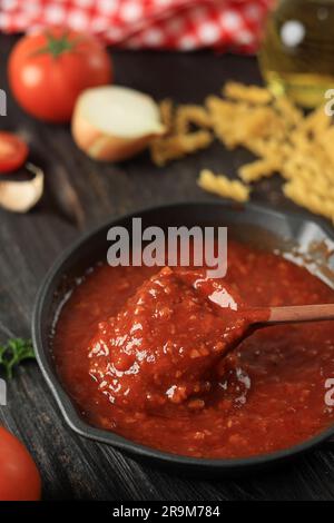Rühren Sie Tomatensoße mit einem Holzlöffel in einer Pfanne aus Gusseisen um Stockfoto