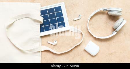 Tasche mit tragbarem Solarpanel, kabellosen Kopfhörern und Kopfhörern auf Grunge-Hintergrund Stockfoto