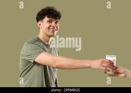 Junger Mann, der ein Glas Milch auf grünem Hintergrund nimmt Stockfoto