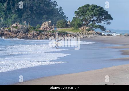 Tauranga Neuseeland - 26 2023. Juni; Surfer im Neoprenanzug mit Surfbrett vom Meer und den Strand hinauf. Stockfoto