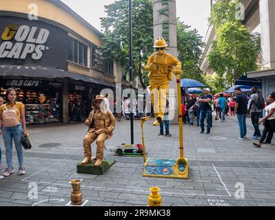 Medellin, Antioquia, Kolumbien -21 2022. November: Aufführung von Straßenkünstlern, einer Frau mit Goldbezug, die einen Hut und eine Brille trägt und einem Mann in einem vollen Stockfoto