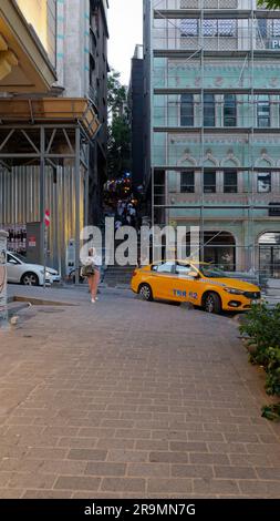 Leute, die abends im Viertel Galata Treppen hinaufgehen, während ein gelbes Taxi wartet und eine Frau ihr Telefon überprüft. Istanbul Türkei Stockfoto