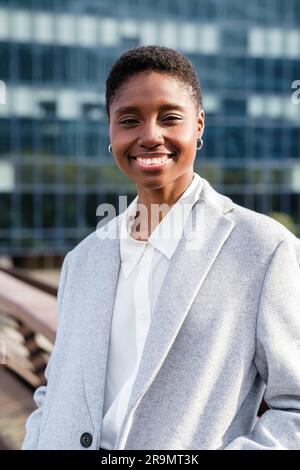 Vertikales Porträt einer jungen afrikanerin, die auf einer Brücke des Finanzdistrikts wohnt. Sie sieht in die Kamera und lächelt Stockfoto
