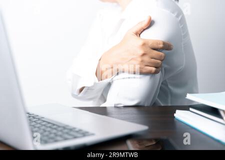 Eine Büroangestellte ist eine Asiatin, die vor dem Laptop sitzt. Eine Geschäftsfrau, die ihren Körperteil mit Fingern, Händen und Armen belastet. A f Stockfoto