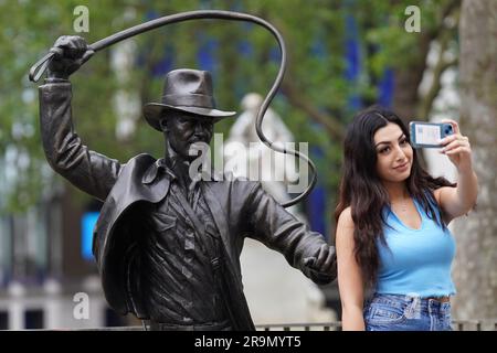 Eine Person, die ein Selfie mit einer lebensgroßen Bronzestatue der Figur Indiana Jones macht, die als neueste Ergänzung des Leicester Square Statue Trail „Scenes in the Square“ enthüllt wurde, Den Helden verewigt, den Harrison Ford mit seiner Peitsche und seinem Fedora aus dem Film "Jäger des verlorenen Schatzes" von 1981 spielte. Bilddatum: Mittwoch, 28. Juni 2023. Stockfoto