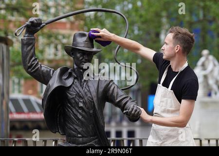 Eine lebensgroße Bronzestatue der Figur Indiana Jones, die gereinigt wird, während sie als neueste Ergänzung der Statue „Scenes in the Square“ auf dem Leicester Square enthüllt wird. Sie verewigt den Helden, den Harrison Ford mit seiner Peitsche und seinem Fedora aus dem Film „Jäger der verlorenen Arche“ von 1981 spielte. Bilddatum: Mittwoch, 28. Juni 2023. Stockfoto