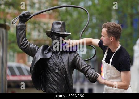 Eine lebensgroße Bronzestatue der Figur Indiana Jones, die gereinigt wird, während sie als neueste Ergänzung der Statue „Scenes in the Square“ auf dem Leicester Square enthüllt wird. Sie verewigt den Helden, den Harrison Ford mit seiner Peitsche und seinem Fedora aus dem Film „Jäger der verlorenen Arche“ von 1981 spielte. Bilddatum: Mittwoch, 28. Juni 2023. Stockfoto