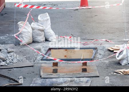 Öffnen Sie die Schachtabdeckung auf der Straße, und reparieren Sie die Straße. Abwasserunfallkonzept Stockfoto