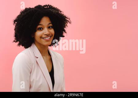 Porträt einer jungen schwarzen Frau mit pinkfarbener Jacke, die vor pinkfarbenem Studiohintergrund lächelt Stockfoto