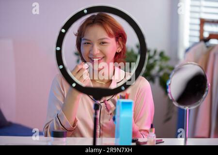 Lächelnde junge Transgender-Frau, die sich selbst filmt und Make-up aufträgt Stockfoto