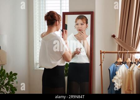 Transgender-Frau, die roten Lippenstift auf Spiegelwein aufträgt und sich für die Arbeit fertig macht Stockfoto