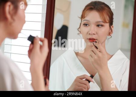 Junge Transgender-Frau, die beim Auftragen von rotem Lippenstift in den Spiegel schaut Stockfoto