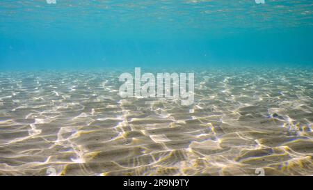 Sandiges, flaches Wasser in der Sonne und Blendung auf dem Meeresboden. Sonnenlicht durchdringt die Oberfläche von türkisfarbenem Wasser und blendet auf sandigem Boden in seichtem Wasser Stockfoto