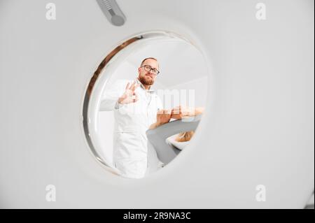 Medizinische Computertomographie oder MRT-Scanner. Männlicher Radiologe untersucht weibliche Patientin und zeigt ok-Gestenkonzept moderner Diagnostik. Stockfoto