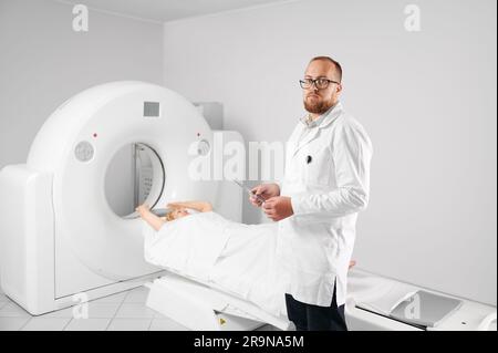 Medizinische Computertomographie oder MRT-Scanner. Porträt der Arzthaltung und Untersuchung der MRT-Ergebnisse. Patientin liegt auf der Couchette. Konzept der Medizin, des Gesundheitswesens und der modernen Diagnostik. Stockfoto