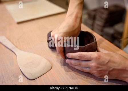 Nahaufnahme von Frauen Töpferhänden funktioniert mit Ton und Keramik, Handwerkerhänden. Kneten und befeuchten Sie den Ton vor der Arbeit in der Keramik- und Keramikwerkstatt Stockfoto