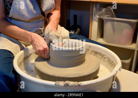 Nahaufnahme der Hände einer Frau aus Keramik, die Lehm auf der Drehmaschine oder dem Töpferrad in einer Töpferwerkstatt bearbeitet und geformt Stockfoto