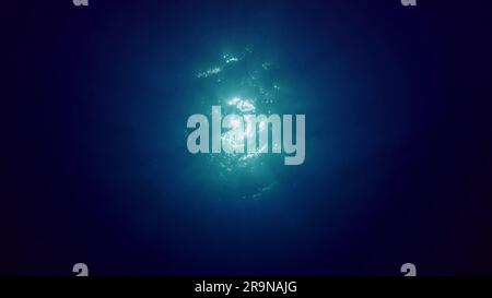 Blick auf Sonnenlicht aus blauem Abgrund, Zeitlupe. Das Licht filtert durch blaues Wasser nach unten. Unterwassersonnenstrahlen im tiefen Ozean. Unterwasserlicht, Sonnenlicht Stockfoto