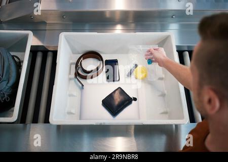 Sicherheitskontrolle am Flughafen vor dem Flug. Passagier hält Plastiktüte mit Flüssigkeiten über dem Behälter mit persönlichen Gegenständen. Stockfoto