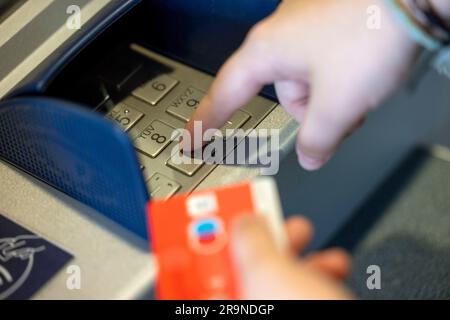 ILLUSTRATION - 23. Juni 2023, Nordrhein-Westfalen, Königswinter: Eine Bankkunden verwendet ihre Giro-Karte mit dem girocard-Logo (r) und dem rot-blauen Maestro-Logo (2-r), um Bargeld von einem Geldautomaten abzuheben. Die Maestro-Funktion der Giro-Karten, die Zahlungen und Barabhebungen im Ausland ermöglicht, wird in Zukunft nicht mehr auf neuen Karten verfügbar sein. Ab dem 1. Juli 2023 werden keine neuen Maestro-Karten mehr ausgestellt. Foto: Thomas Banneyer/dpa Stockfoto