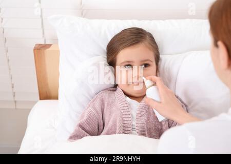 Mutter benutzt Nasenspray, um ihre kleine Tochter im Bett zu behandeln Stockfoto