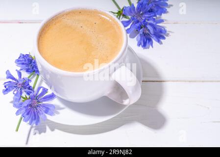 Kräuterkaffee aus Zichorien und blaue Blumen auf einem weißen Holztisch. Alternativer veganer und Keto-Diät-Kaffee mit Zichorienblüten und Wurzelpulver Stockfoto