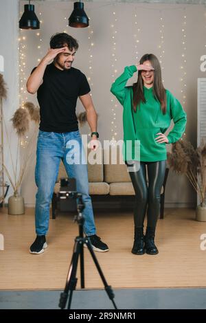 Voller Körper von fröhlichen jungen Männern und Frauen in lässiger Kleidung, die neben einer Fotokamera stehen und Videos für einen Modevlog aufnehmen Stockfoto