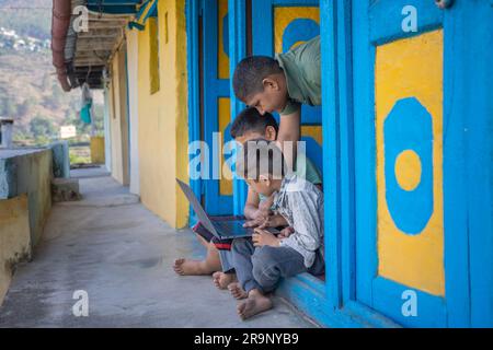 Asiatisch-indische Landkinder lernen zusammen auf einem Laptop, während sie auf dem Türrahmen sitzen, e-Learning-Konzept, lernen von zu Hause aus Stockfoto