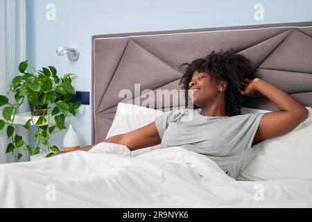 Glückliche afrikanische lächelnde Frau, die sich morgens auf dem Bett ausstreckt. Sie wachen aus einem erholsamen Schlaf auf. Stockfoto