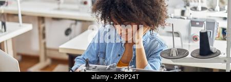 Die afroamerikanische Designerin zeichnet mit Nähmaschine und Laptop Skizzen am Tisch Stockfoto