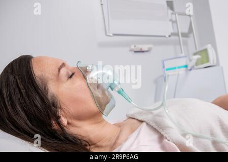Eine Erwachsene Frau liegt in einer Sauerstoffmaske auf einem Krankenhausbett und wird behandelt. Stockfoto
