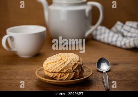 Szene der Teezeit mit einem kleinen, hausgemachten runden Kuchen gefüllt mit Blaubeercreme in einem Holzgericht mit einer weißen Keramiktasse Tee und Metalllöffel Stockfoto