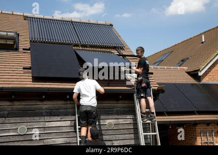 Zwei Techniker installieren schwarze 410kW-Perlitplatten auf einem Ziegeldach, das bereits über einen Satz evakuierter ET-Rohre für die Solarwasserheizung bei Coleman verfügt Stockfoto