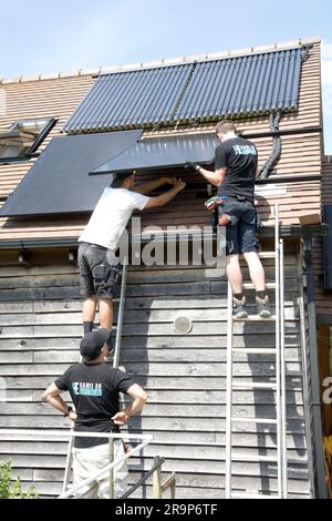 Zwei Techniker installieren schwarze 410kW-Perlitplatten auf einem Ziegeldach, das bereits über einen Satz evakuierter ET-Rohre für die Solarwasserheizung bei Coleman verfügt Stockfoto