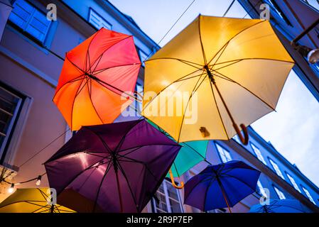Farbenfrohe Sonnenschirme schmücken eine enge Straße zwischen alten gelben europäischen Gebäuden. Bunte Sonnenschirme sorgen für eine festliche, lustige Kulisse in Wien Stockfoto