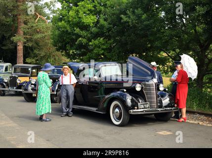 Ein Chevrolet-Auto aus dem Jahr 1938 mit Leuten in historischen Kostümen am Bahnhof Arley an der Severn Valley Railway. Stockfoto