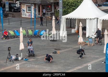 Kaiserslautern, Deutschland. 28. Juni 2023. Fußgänger genießen es, Künstler bei der Arbeit auf dem Stiftsplatz (Platz) zu beobachten. Elf internationale Künstler aus 6 Ländern verwandeln den Stiftsplatz (Platz) in dreidimensionale Kunst. 3D Street Art nutzt die Perspektive, um eine optische Illusion des Weltraums zu erzeugen. Besucher können alle Künstler an drei Tagen bei der Arbeit beobachten, von Mittwoch um 8:00 UHR bis Freitag um 6:00 Uhr. Das diesjährige Thema ist „Digitalisierung und intelligente Stadt“. Gemälde zeigen Roboter, Daten oder Cyberpunk-Szenarien. Kredit: Gustav Zygmund/Alamy News Stockfoto