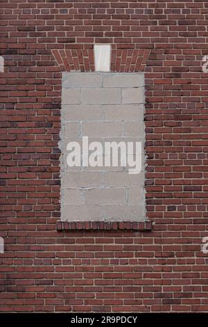 Fenster, das mit Betonblöcken an einer roten Backsteinwand versiegelt ist, mit einem dekorativen Backstein-Fensterkopflintel in Form eines flachen Bogens mit Marmorsteinpflaster Stockfoto