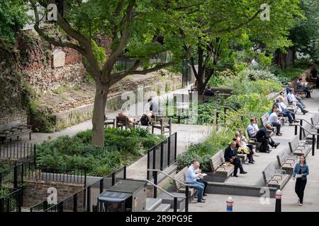 Stadtarbeiter genießen den relativen Frieden der modernen Metropole im St Alphage Garden unter den Überresten der alten römischen Mauer (links), die einst die Grenze der antiken Stadt Londinium bildete - aber heute mit der Quadratmeile aus dem 21. Jahrhundert der Stadt London, Das Finanzviertel der Hauptstadt am 27. Juni 2023 in London, England. Die römische Mauer wurde zwischen 190 und 225 als defensive Mauer aus Stein um die Landseite der Stadt errichtet. Die Londoner Mauer war eines der größten Bauprojekte, die in römischem Großbritannien durchgeführt wurden und etwa 85.000 Tonnen Kent erforderten Stockfoto