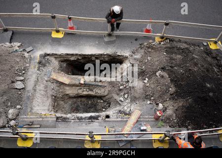 Luftaufnahme von zwei Bauunternehmern, die während der Gaswerke in der Fore Street in der City of London, dem Finanzviertel der Hauptstadt, am 27. Juni 2023 in London, England, in ein Loch auf der Straße blicken. Stockfoto